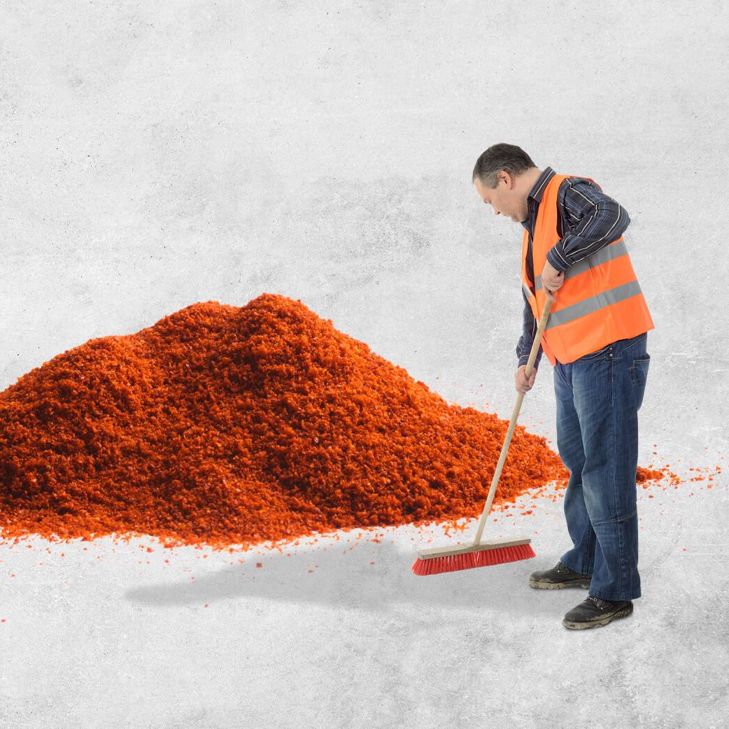 Man in hi vis sweeping up a large pile of orange dust with a broom